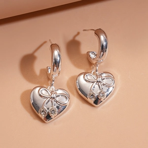 Detail of silver heart earrings featuring delicate bows and sparkling zircon stones