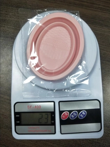 Pink silicone makeup brush cleaner mat in packaging on a scale weighing 23 grams