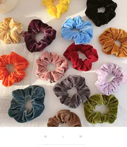 Flat lay of 13 colorful velvet scrunchies displayed on decorative vintage newspaper