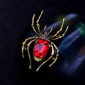 Macro view of a gold spider brooch with a large red gemstone on a black textured surface