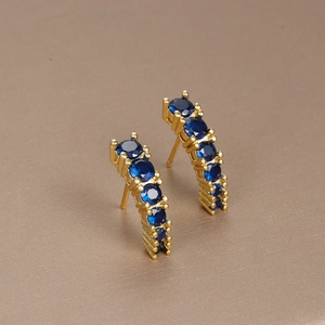 Detailed close-up of gold curved earrings featuring brilliant dark blue round gemstones