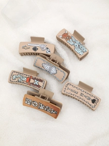 Detailed view of beige and brown Western cowboy style hair clips with cactus and boot patterns