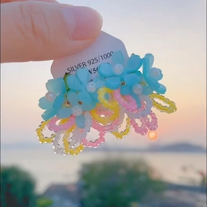 Detail of flower earrings with colorful beads held against a sunset beach backdrop