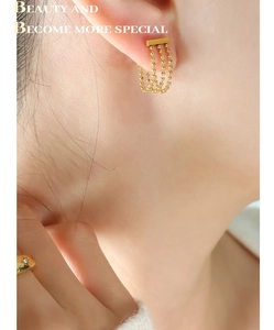 Détail de boucles d'oreilles en titane doré avec triple chaîne à billes et pompons