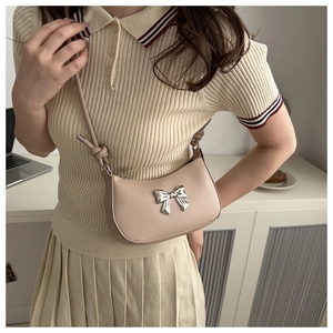 Close-up of beige shoulder bag featuring a metallic silver bow and knot strap detail