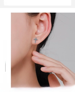 Close-up of vintage silver cross stud earrings with turquoise stones on model ear