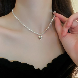 Detail of silver heart pendant necklace with mixed pearl and square link chain on model