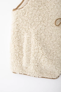 Détail du gilet en polaire beige avec bordure marron et texture en laine de mouton