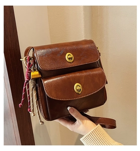 Close-up of retro brown crossbody bag with dual metal turn-lock buckles and woven tassel