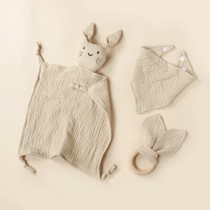 Three-piece beige cotton muslin baby set with rabbit comforter, bib, and wooden teether