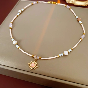 Detail of beaded necklace with gold sunflower pendant and pink stone center on gray base
