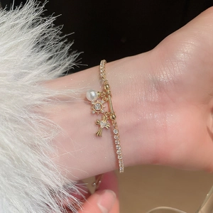 Detailed shot of gold fleur-de-lis cross bracelet with zircons and a pearl charm