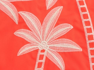 Detailed macro shot of palm tree embroidery on orange fabric with geometric patterns