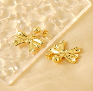 Close-up of golden bow-knot earrings on silk with high-gloss polished metallic finish