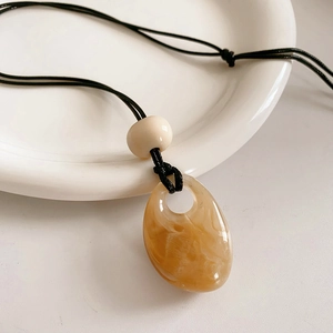 Macro view of amber resin drop pendant with marble texture on minimalist woven cord