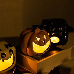 Ceramic Halloween pumpkin and bat candle holders on books with warm interior lighting