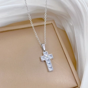 Detail of silver cross pendant featuring square zirconias on beige jewelry box