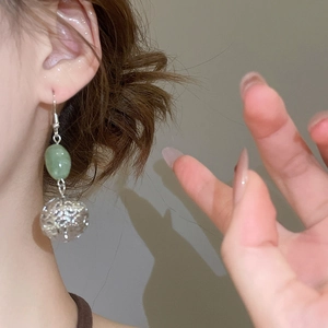 Gros plan d'une boucle d'oreille avec perle verte et sphère argentée sur l'oreille