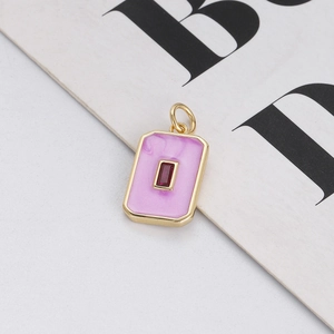 Macro detail of gold rectangle pendant with pink enamel and deep red gemstone