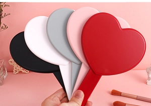 Detail view of five heart-shaped handheld makeup mirrors in various colors being held