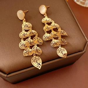 Detailed view of golden multilayer hollow leaf earrings with white opal on a jewelry box