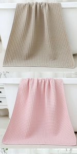 Detail of beige and pink waffle weave cotton bath towels hanging on a bathtub