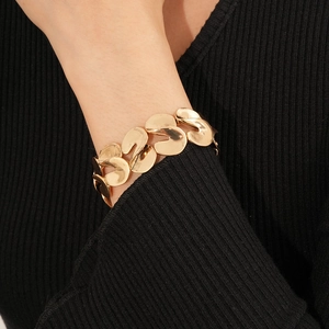 Close-up of a wide gold-tone metal bracelet with irregular geometric linked disks