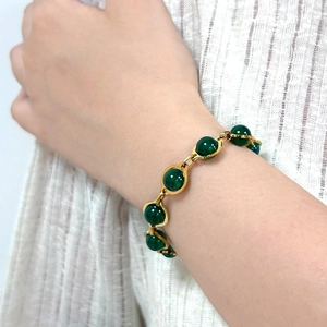 Detailed close-up of retro gold bracelet with polished green round beads on wrist