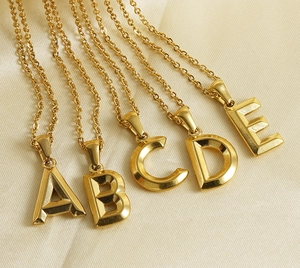 Detail of 18K gold-plated 3D initial necklaces A to E on elegant silk fabric
