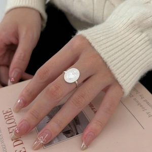 Detail of 925 silver shell heart ring worn by model over a soft pink magazine