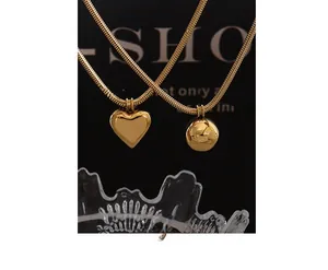 Detail of gold-plated snake chain with polished heart and sphere pendants on black background