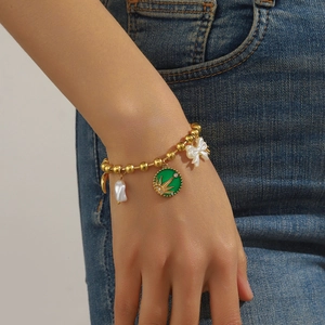Gold-plated beaded bracelet with green enamel sun pendant, pearls and bow on model wrist