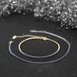Macro detail of silver and gold tennis bracelets with vibrant blue zircons on black surface