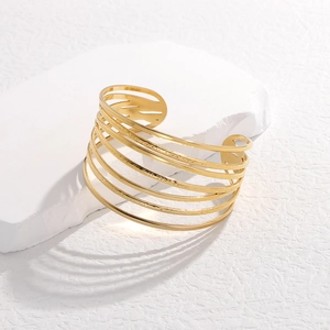 Macro detail of wide gold stainless steel cuff featuring multilayer hollow wave design