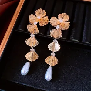 Orecchini a fiori dorati con zirconi e pendenti di perle bianche su velluto nero