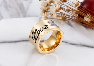 Macro detail of golden wide band ring with black Love lettering and heart cubic zirconia