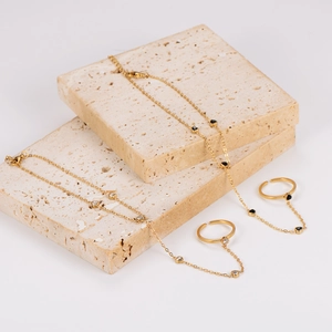 Elegant gold-plated hand chain with white zircon and black heart charms on stone stands