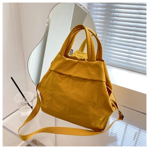 Detailed view of ginger yellow nylon tote bag with pleated texture on acrylic table