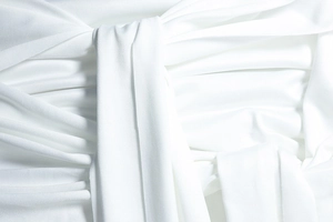 Detail shot of white off-shoulder dress featuring intricate pleats and tied ribbon accents