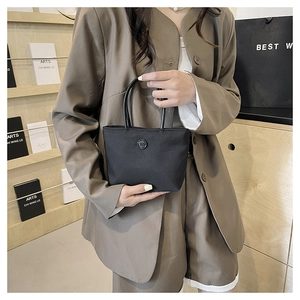 Détail d'un sac seau noir en nylon avec logo m, tenu par un mannequin en tailleur chic
