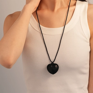 Détail d'un pendentif cœur noir vintage avec texture tissée sur collier long