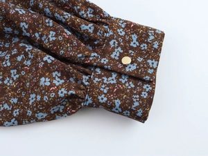 Detail of floral chiffon sleeve with brown pattern and decorative gold metal button