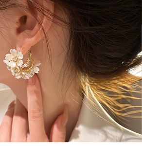 Dettaglio degli orecchini a cerchio a C floreali con petali bianchi e finitura oro