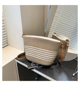 Detail of hand-woven straw bag with white stripes and brown leather strap on a desk