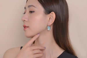 Close-up of model wearing elegant heart-shaped blue gemstone earrings with silver hooks