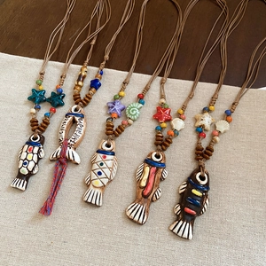 Handmade ceramic fish pendant necklace with sea star beads on rustic linen background