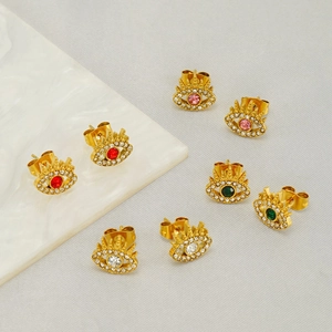 Gold evil eye earrings with colorful zircon stones on marble and fabric background