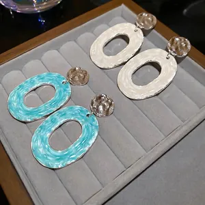 Textured oval drop earrings in lake blue and off-white enamel on a grey velvet tray