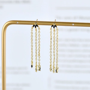 Detailed view of luxury gold tassel earrings with black leaf accents and triple chain design