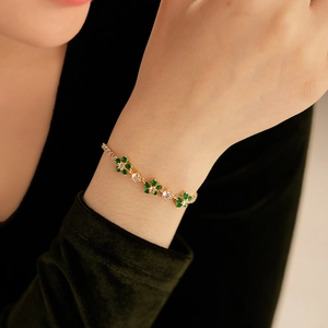 Detail of a floral gold bracelet featuring emerald green petals and a crystal center